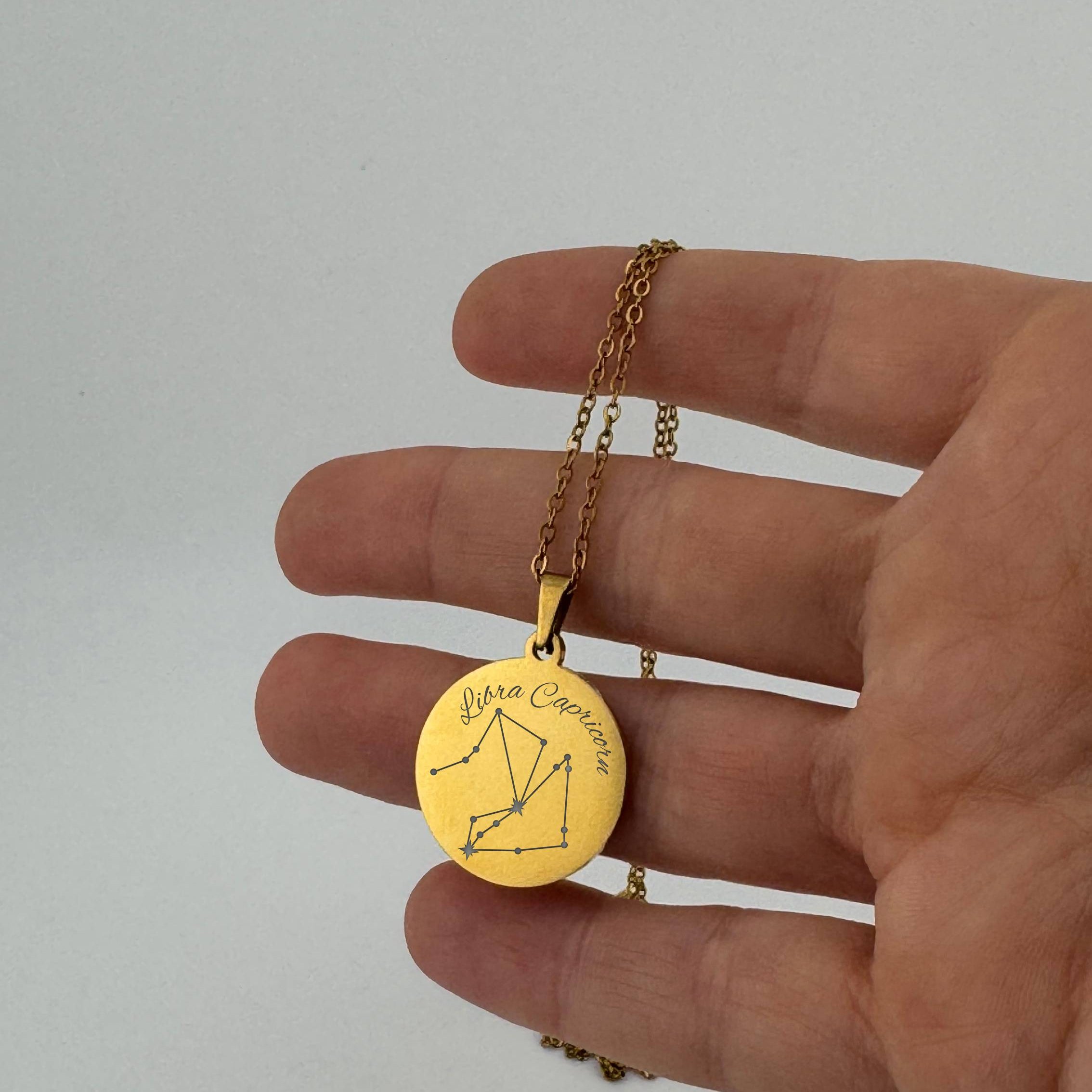 Gold Libra and Capricorn constellation necklace with sign names engraved, held in hand