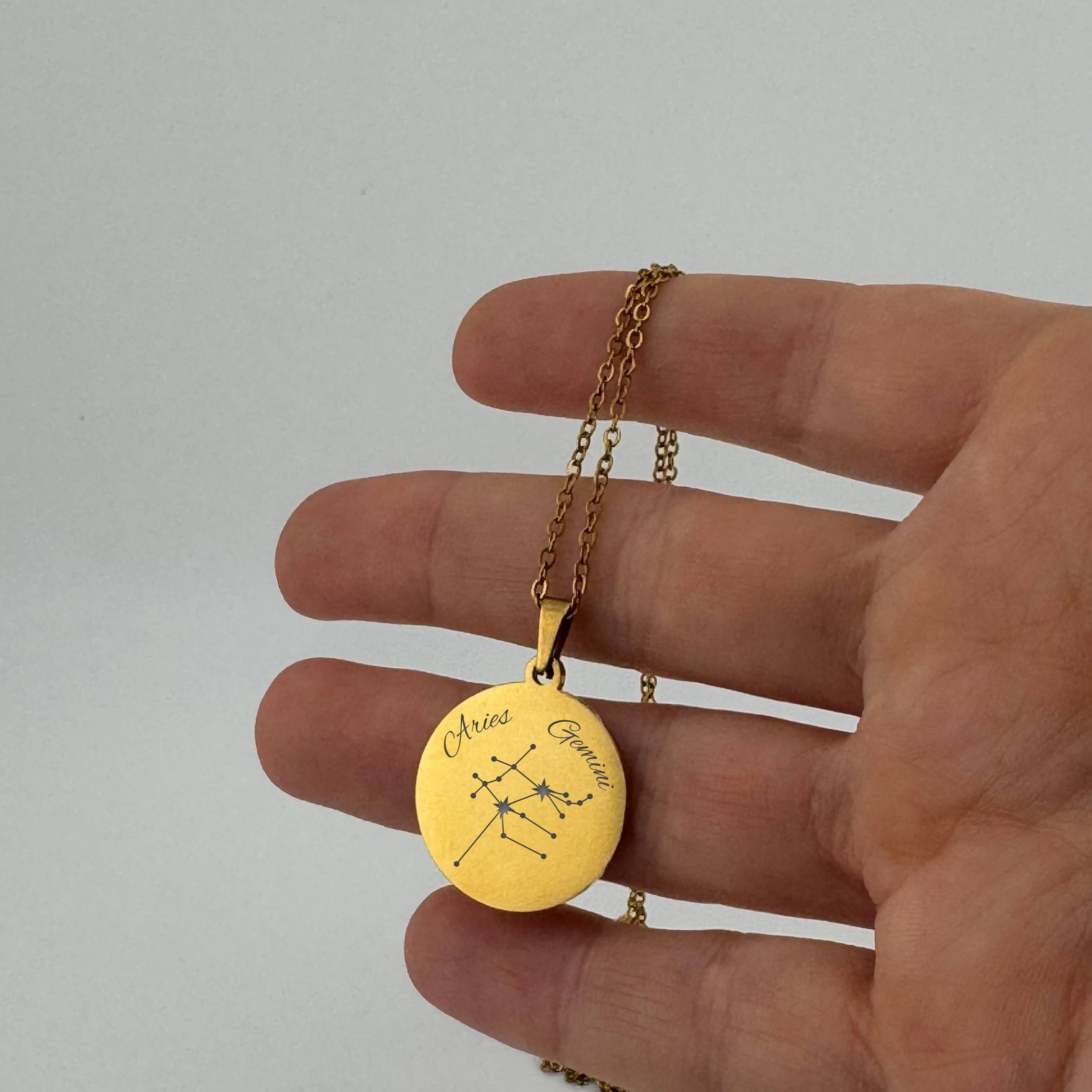 Gold Aries + Gemini constellation necklace with sign names engraved, held in hand