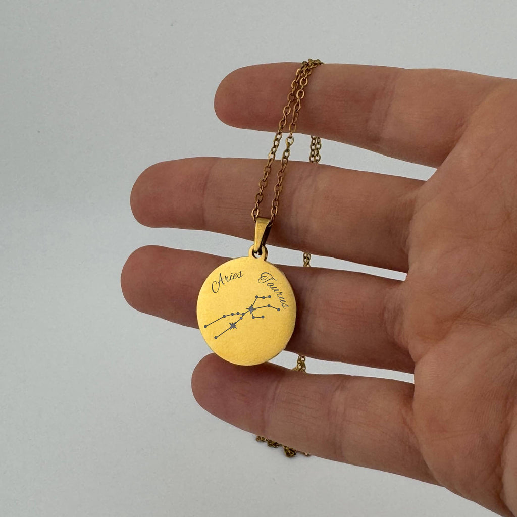 Gold Aries  + Taurus constellation necklace with sign names engraved, held in hand
